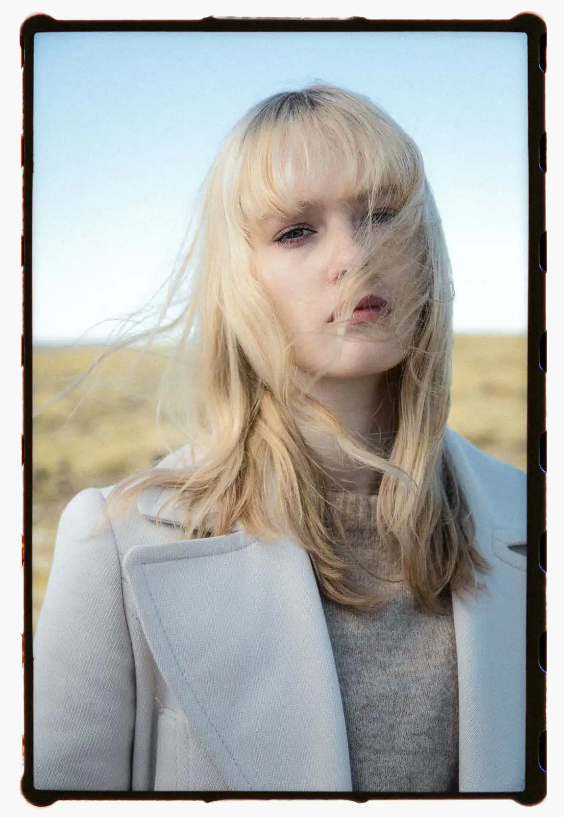 Close portrait of a young blonde woman outdoors with wind moving through her hair photographed on analog film against an open landscape and pale sky