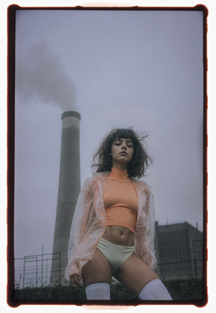 Analog portrait titled Chords of a model in bold fashion against an industrial smokestack backdrop.