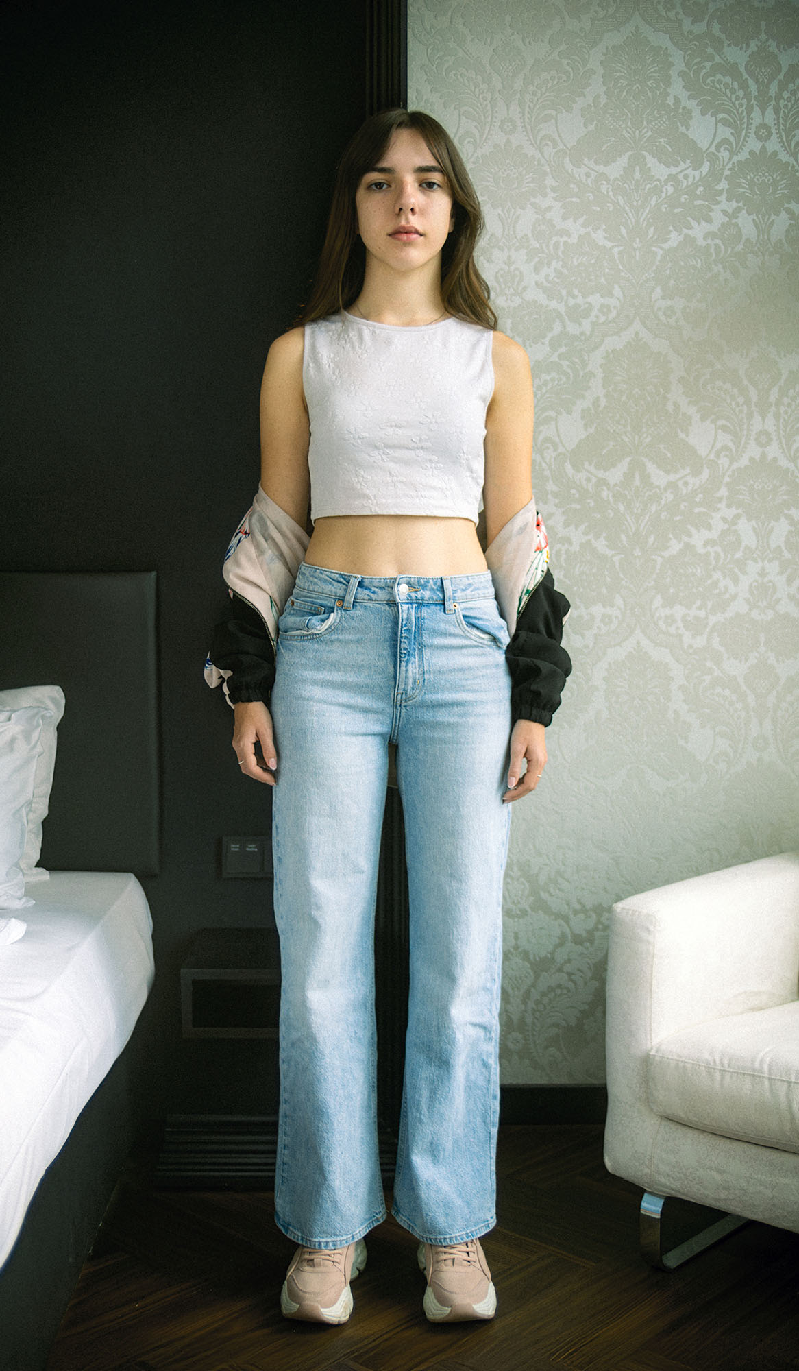 Conceptual fashion portrait of a young woman posed uncomfortably in a staged interior.